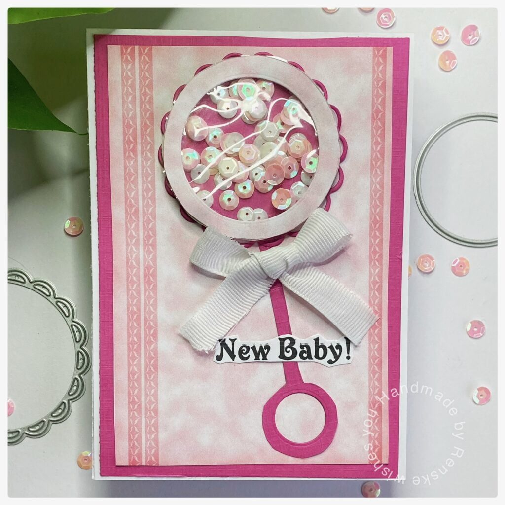My finished baby rattle card with lots of pink on the digital design paper and a rattle shaker on top.