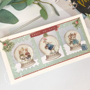 Top view of a handmade Christmas card featuring three snow globes with festive scenes, surrounded by holiday decorations and details.
