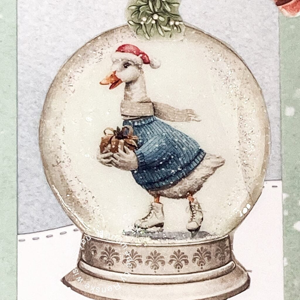 Close-up of a snow globe featuring a goose holding a gift in a festive scene, part of a handmade Christmas card.