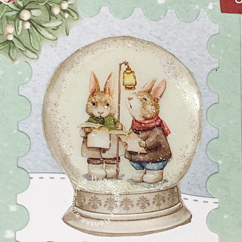 Close-up of a snow globe showcasing singing rabbits in a festive scene, part of a handmade Christmas card.