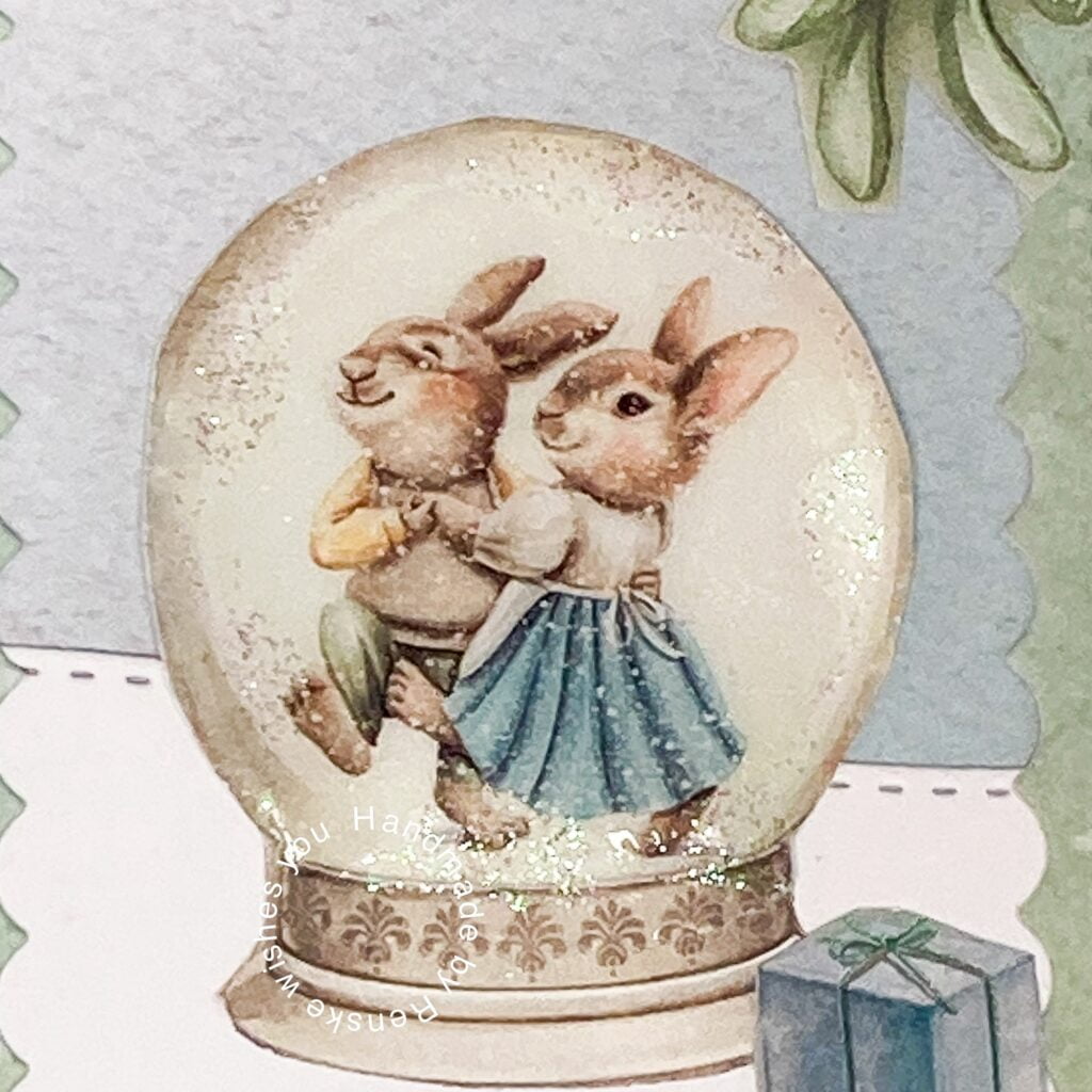 Close-up of a snow globe featuring two dancing rabbits in a festive scene, part of a handmade Christmas card