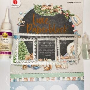 Assortment of crafting materials laid out for making a DIY snow globe Christmas card: luxe paper block, scissors, slimline dies, paper glaze, glitter glue, and decorative elements.