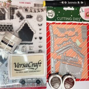Assortment of materials used for crafting a Christmas market card: die-cut elements, colored paper, ink pads, deco snow, and crafting tools