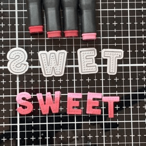 Photo displaying alphabet dies, alcohol markers, and gradient-coloured letters spelling 'Sweet.