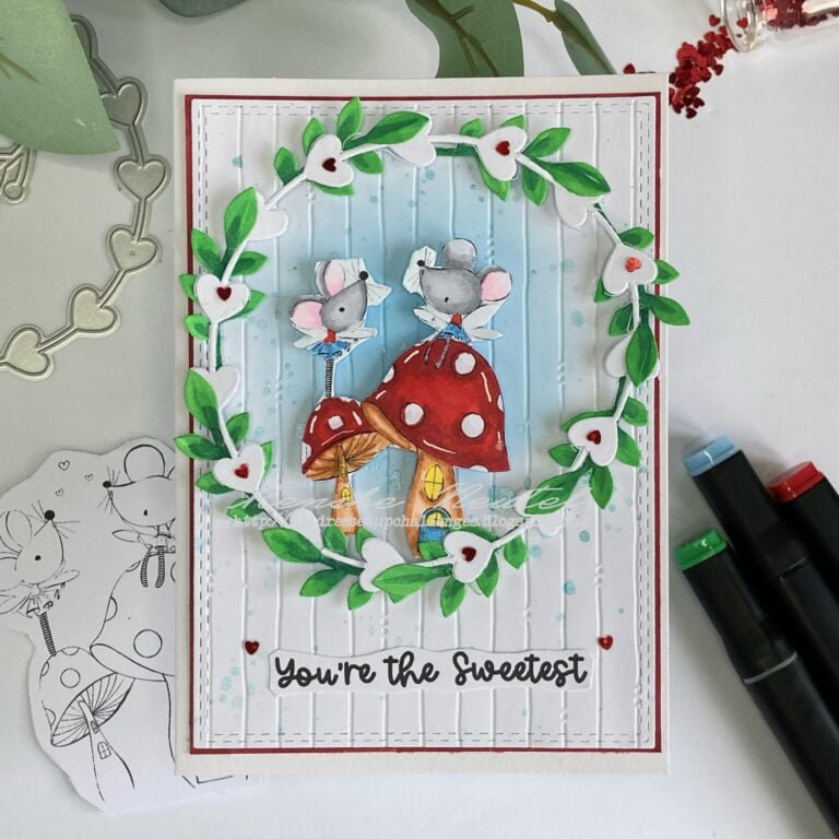 Featured image of a cute handmade Valentine's Day card with adorable fairy mice, surrounded by a frame/wreath with colorful leaves and red heart embellishments. The card is set against a dreamy blue background with embossed texture, showcasing creativity and love in crafting.