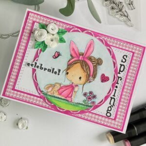 Bunny Hairband All Dressed Up Stamps handmade spring card other angle This image provides a top-down view of the entire handmade spring card, but the card is positioned at a slight angle. Despite the angle, the card's charming design and vibrant colours are still clearly visible. The Bunny Hairband digital stamp takes center stage, surrounded by layered elements and decorative embellishments. This photo offers a unique perspective on the card's composition and design, showcasing its whimsical beauty.