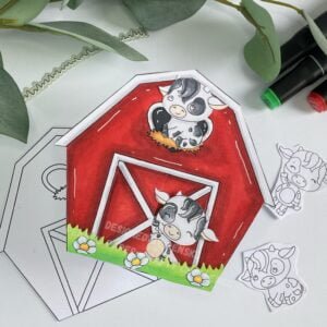 Handmade cow greeting card in a barn shape with streamside studios 1 Cow greeting card displayed at an angle, showcasing the entire card design with whimsical barn shape and farm-themed elements. The barn is primarily red with white highlights, and the cows feature black and white patches. reen grass and blue flowers add color and detail to the scene.