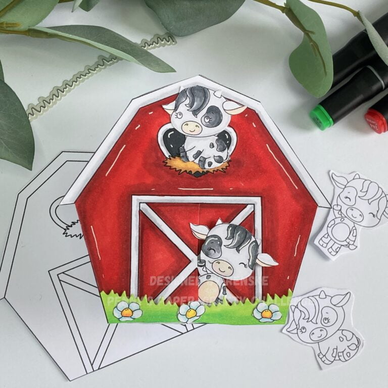 Cow greeting card in barn shape with farm theme. Full view of the front of the card, featuring a charming cow illustration waving from a barn door frame. Above the door is a heart-shaped window filled with hay, where another cow is sitting. The barn is predominantly red with accents of white, while the cows are depicted in shades of grey. reen grass and blue flowers add color and detail to the scene.