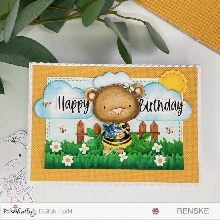 Aerial view of the entire card featuring a handmade spring birthday card. The card showcases a charming spring scene with a bear holding gifts surrounded by grass, a fence, clouds, and a sun.