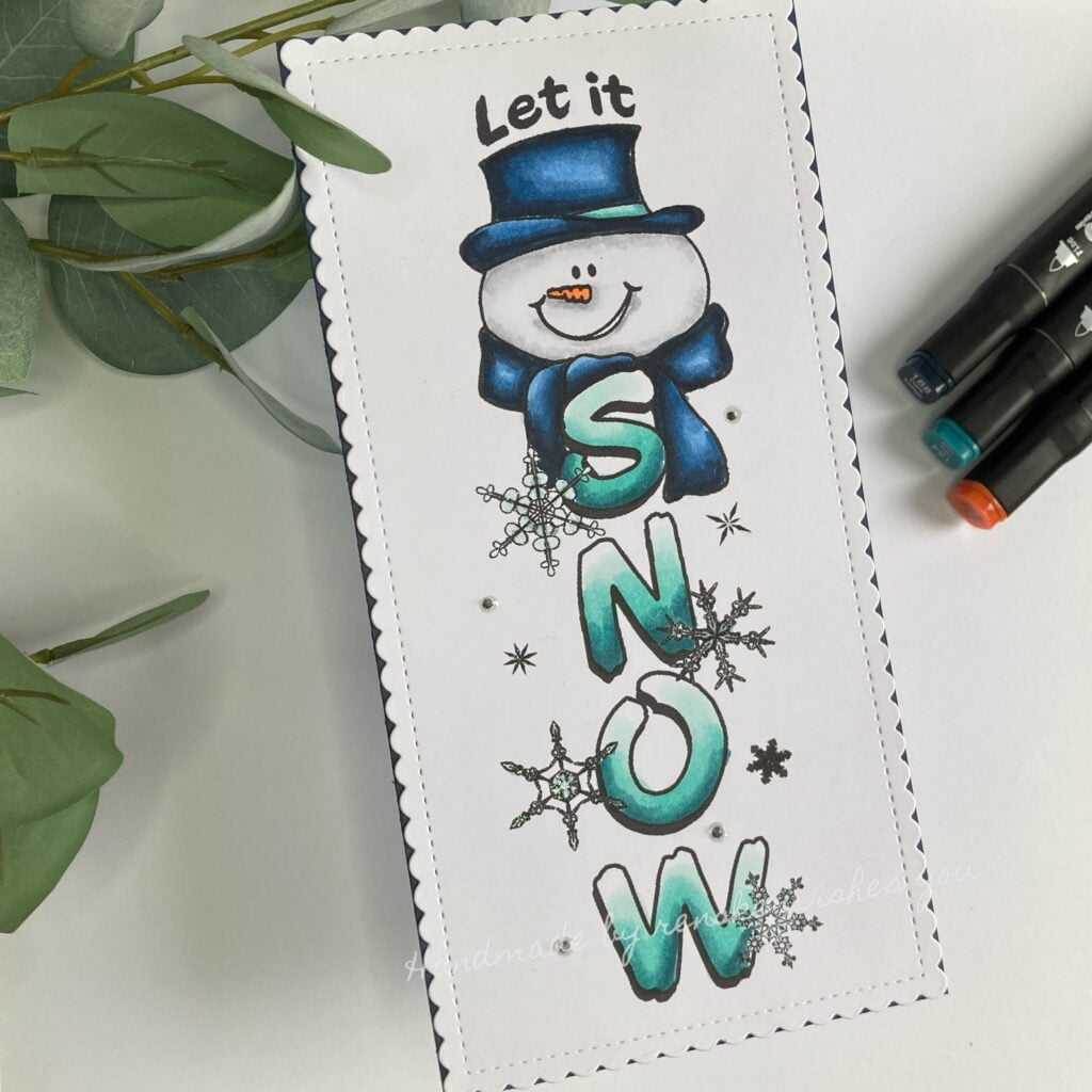 Top-down view of the completed handmade snowman winter card featuring a charming snowman design with the lettres snow captured at an angle. The card showcases the snowman stamp coloured with alcohol markers with colours of teal and blue