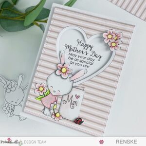Handmade Mother's Day Card Bunny Rabbit Polkadoodles (2) Top-down view of a handmade Mother's Day card featuring a bunny holding a blank greeting card surrounded by flowers. The card is positioned diagonally, allowing for a clear view of the entire design.