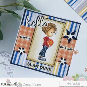 Angled overhead view of DIY basketball card with 'Basketball - Little Dudes' digital stamp. The card is positioned diagonally, allowing a comprehensive view of the design. Layers of patterned papers and a handcrafted sentiment complement the central image of a basketball player, creating a dynamic visual composition.