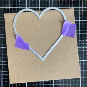 Die-cut the base card in a heart shape a heart shaped die with tape on a square piece of kraft paper. The top of the heart shape die is above the fold line.