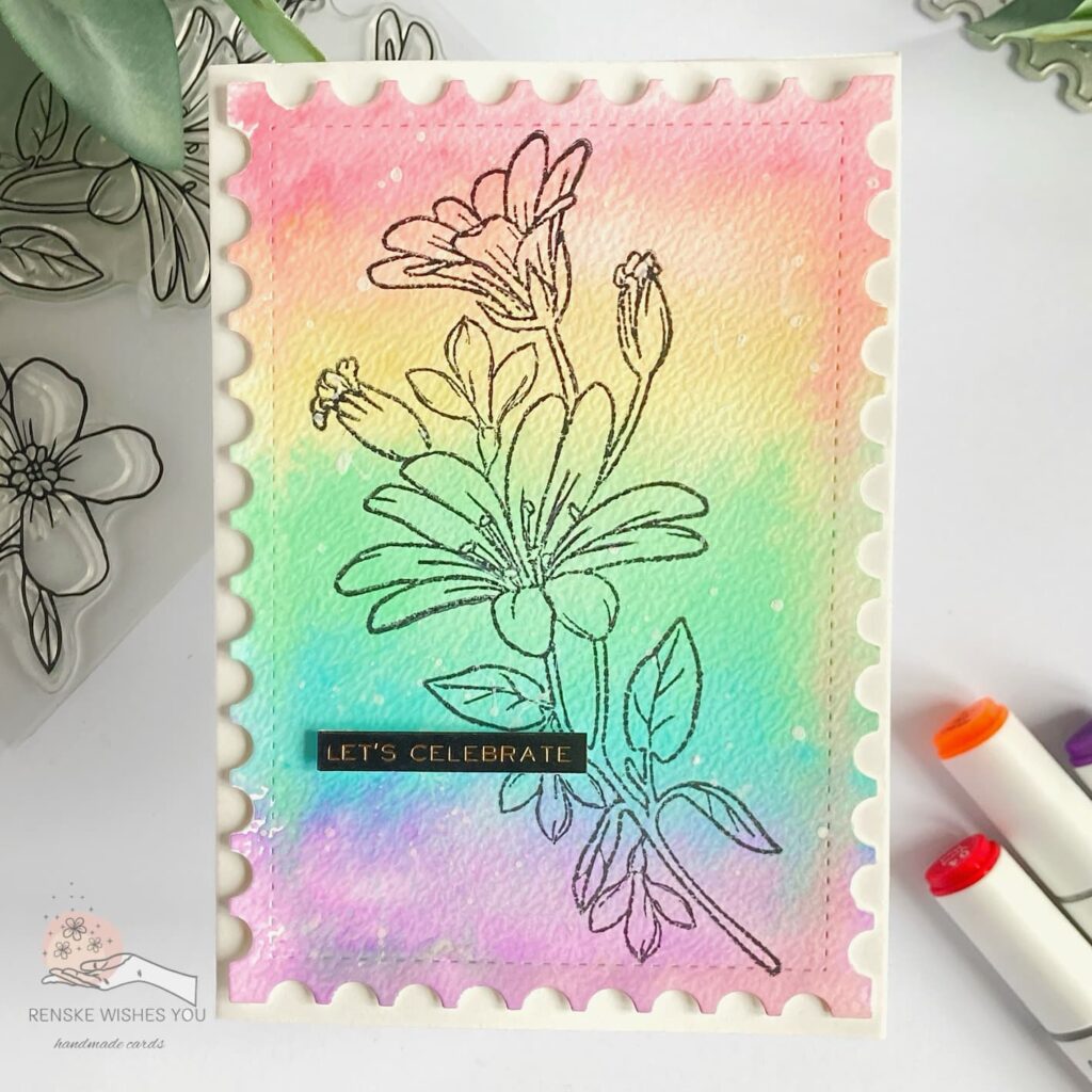 Overhead view of a watercolour flower card laying flat and straight. The card features a rainbow watercolour background with a stamped black floral design and a 'Let's Celebrate' sentiment.