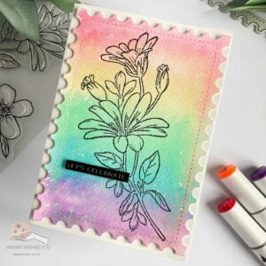 Overhead view of a watercolour flower card laying flat at an angle. The card showcases a vibrant rainbow watercolour background, a black stamped floral design, and a 'Let's Celebrate' sentiment.