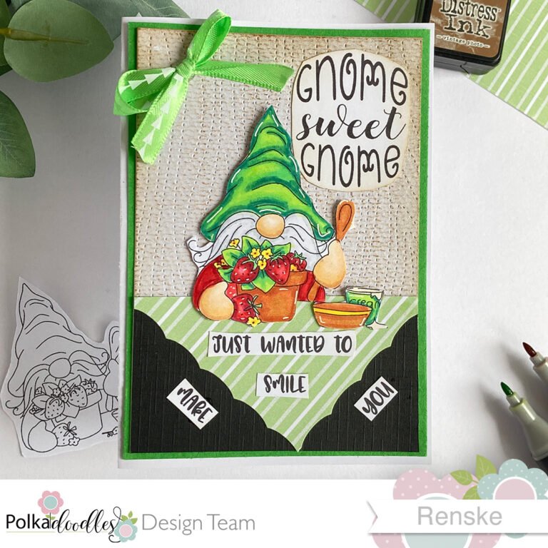 A top-down view of a strawberry gnome card lying flat and centered in the image. The card features a charming gnome holding a pot of strawberries, with a cozy background and vibrant colors.
