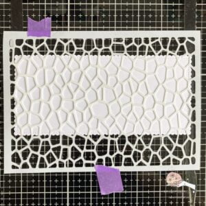 Picture of the stencil laying on the white paper Stencil taped over white panel for creating a summer themed card with a swimming pool background.