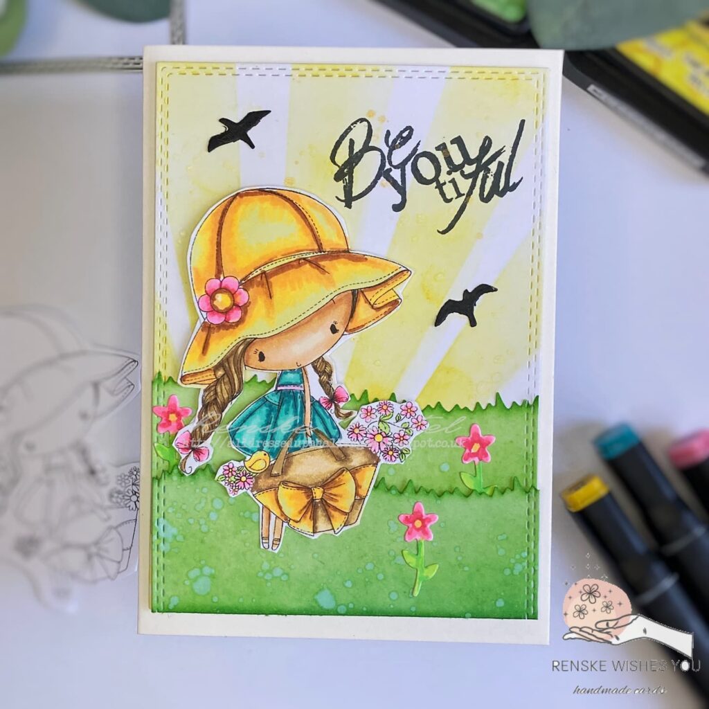 Flat lay view of the completed Flower Girl card, showing the entire card design. The card features a vibrant Flower Girl in a sunny hat and teal dress, surrounded by colorful flowers and a background with sunbeams and grassy layers."