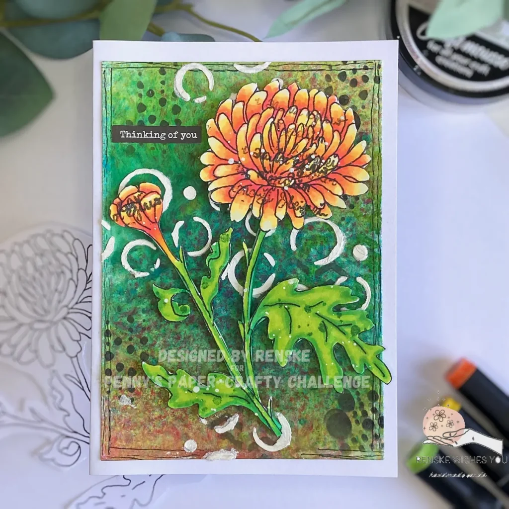 Top-down view of a handmade mixed media flower card lying flat and centered. The card features a brightly colored chrysanthemum in shades of yellow, orange, and red, placed on a textured, layered background created with acrylic sprays and stencils. A sentiment in the top left reads 'Thinking of You.