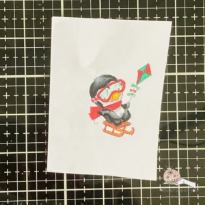 Coloured digital stamp Waddy on a sleigh lose-up of Waddy Penguin on a sleigh, coloured and cut out, ready to be added to a festive tag. The intricate details and dimension bring a playful holiday feel to the image.