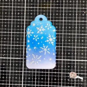 Finished background Penguin Christmas tag Custom-made background for a festive penguin tag, featuring an ink-blended gradient from dark to light blue, with textured stars and ice flowers added using a stencil and crafting mousse.