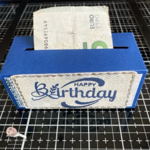 Happy birthday money roll box Front view of the assembled DIY money roll box with 'Happy Birthday' sentiment. The money roll is partially visible, emerging through a slit on the front of the box.