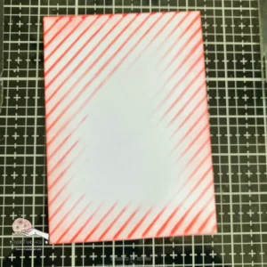 Stencilled background with red and white stripes An image of the finished red and white striped background, showcasing vibrant diagonal stripes that provide a lively contrast for the Hot Chocolate Christmas Card.