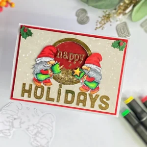 Angled, top-down view of the Christmas shaker card showing the full design with two gnomes from the Crackers digital stamp by Sheepski Designs. The card has a central shaker window, bordered with gold and layered with red and patterned paper for a Christmas-themed look. Stars and holly add embellishment around the window, enhancing the holiday appeal.