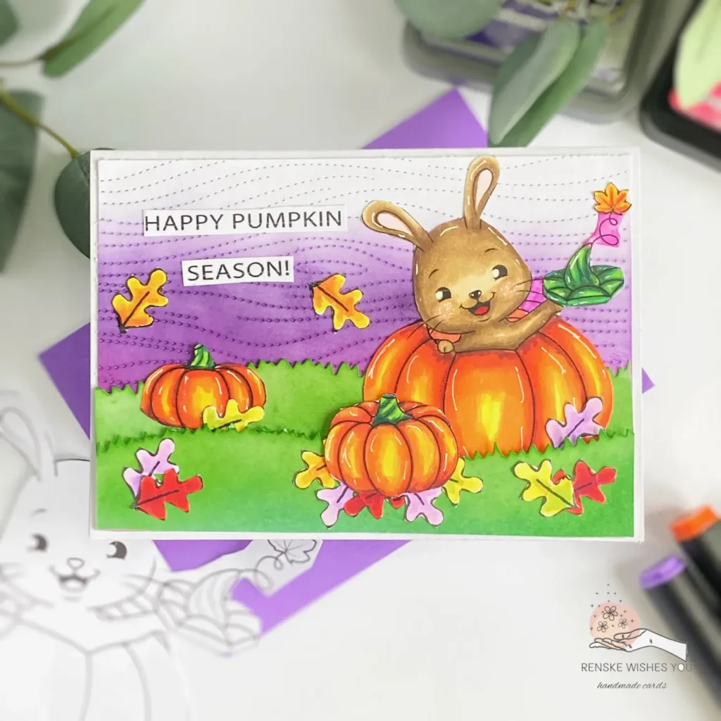 Top-down view of a DIY Pumpkin Card showing the full design with a purple ink-blended background, layered autumn leaves, and pumpkins. A digital stamp with a bunny inside a pumpkin is on the righ of the card, surrounded by rich autumn colours.