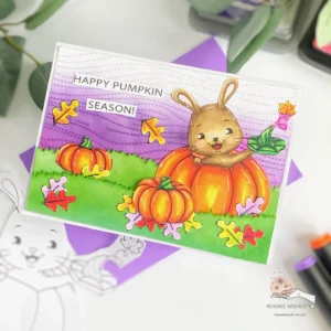 DIY Pumpkin card Isabelcristina Angled Angled top-down view of the full DIY Pumpkin Card. The background features purple tones with layered autumn leaves and pumpkins surrounding a cute digital stamp of a bunny nestled in a pumpkin.