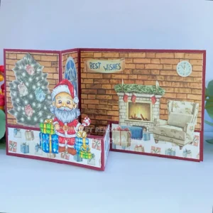 Double Z fold card Christmas Santa is here 1 Angled front view of the Double Z fold card tutorial, focusing on Santa standing on the strip near the Christmas tree on the left panel. The cosy living room scene with a fireplace and the "Best Wishes" sentiment is clearly visible on the right panel.