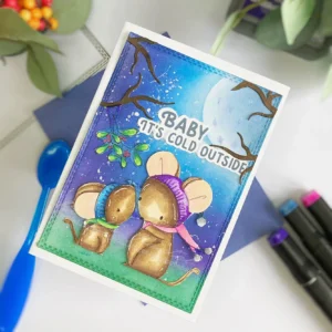 An angled overhead view of a Mice Christmas card, showcasing the two mice under mistletoe against a night sky. The card is tilted slightly, allowing a better view of the soft glowing moon and the details of the background blending. The mice are coloured in shades of brown with their scarves and headbands in contrasting hues, creating a cozy winter scene