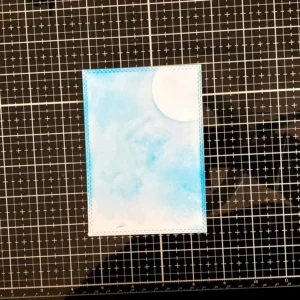 An image showing the beginning of the background creation for the Mice Christmas card. The sky is being inked with distress inks. This is the first layer with Tumbled Glass and Salty Ocean. This is part of the process to create a magical winter night for the mice illustration