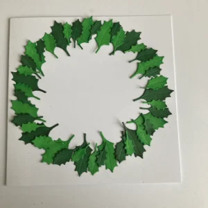 The Holly wreath on the Christmas Hugs card from All Dressed Up Stamps A close-up of the card's base with the holly and berry wreath, created with die-cut leaves and red berries. The wreath is arranged in a circle shape with the 'Happy Holiday' sentiment on vellum in the bottom-right corner. The wreath design frames the spot where the Christmas Hugs digital stamp would be placed