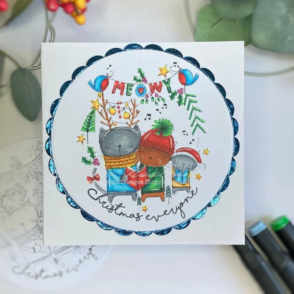 op-down view of a handmade Meowy Christmas card, featuring a festive digital stamp of three cats wearing holiday attire surrounded by a decorative metallic blue border. The card base is white, and the digital stamp showcases vibrant colouring with alcohol markers. Perfect for holiday crafting inspiration.