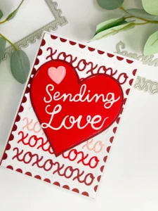 DIY Valentine card Design Aveccreative 2 A top-down angled view of the DIY Valentine card design, highlighting the intricate xoxo card background and the dimensional heart centerpiece with the sentiment “Sending Love.