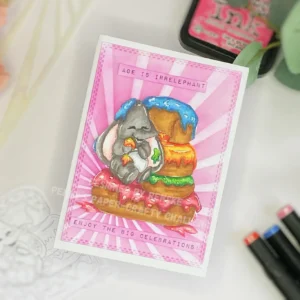 Elephant birthday card with donotus top-down angled view of the elephant birthday card. The card shows a digital stamp of an elephant with doughnuts, pink sunbeam stencilling, and sentiment strips.