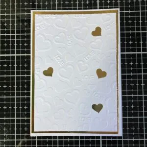 Embossed background with embossed hearts and the word love Close-up of the embossed background in white with the gold behind it, attached to the base of the handmade wedding card. The texture adds elegance to the design, highlighting the craftsmanship of the wedding card. This background is a perfect example of how to elevate an embossed wedding card.