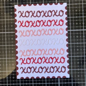 Background with dark red border The completed xoxo card background for the DIY Valentine card design, featuring rows of layered die cuts in a pink, red, and white colour palette.