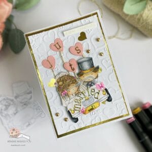 Handmade wedding card with embossing and Wedding Car stamp (2) Overhead angled view of a handmade wedding card with a tilted wedding car and heart-shaped balloons. The playful design is accented with gold elements, making it an ideal example for creating an elegant wedding card. The card's angle shows off the unique design and layers."
