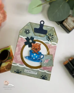 Tea Bag shaped card Tea Time Isabel Cristina 1 Angled top-down view of the tea bag-shaped card, highlighting its textured layers, wave borders, and charming embellishments like flowers and pearls.
