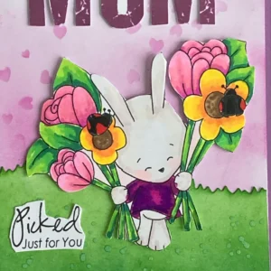 Close up coloured bunny bunch flowers Polakadooes A close-up of the coloured digital stamp on the handmade Mother's Day card. The bunny has soft shading with alcohol markers, featuring light beige fur and rosy pink details. The flowers are a mix of vibrant pink and yellow, with delicate green leaves, creating a cheerful and detailed focal point.