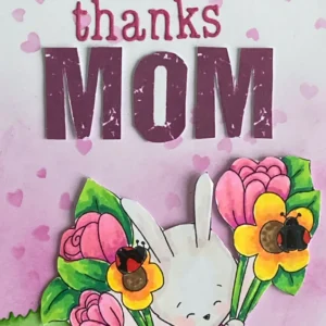Close up sentiment thanks Mom A close-up of the "Thanks Mom" sentiment on the handmade Mother's Day card. The text is created using pink die-cut letters, which contrast against the softly blended pink background and the lettres Mom are in purple. Positioned slightly raised, the letters add depth and a clean, elegant finish to the design.