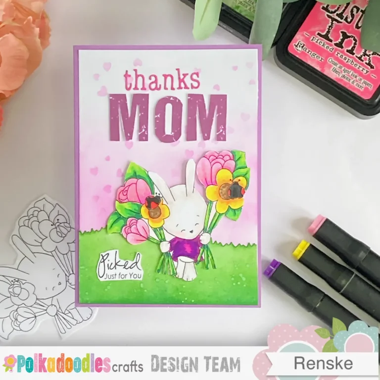 top-down view of the handmade Mother's Day card, featuring a pastel purple card base with a soft pink blended background. The focal point is a cute bunny holding a bouquet of flowers, surrounded by a stencilled heart pattern. A die-cut grass border at the bottom adds texture, and the "Thanks Mom" sentiment is displayed in ourple and pink lettering