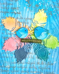 Close up birds on feathers. Close-up of the feather wreath encircling the birds on the mixed media card. The feathers are layered in rainbow colours, creating depth and movement. Ink splatters and subtle script stamping add texture, while the distressed background blends seamlessly into the design. This detailed view highlights the intricate mixed media techniques used to bring the composition together in this mixed media card tutorial.