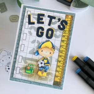 Back to school card with All Dressed Up Stamps back to school boy Overhead view of a back to school card idea featuring a flat-lay display of the finished handmade card. The card includes a layered background with grey cardstock, patterned paper with stencilled numbers, a coloured image of a schoolboy with a ball, and die-cut letters spelling “Let’s Go