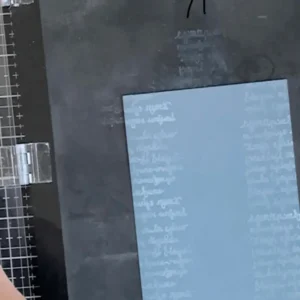 Grey card stock with written text Stamping platform with a piece of blue cardstock layered with soft white handwritten script, great for creating textured backgrounds in a back to school card idea.