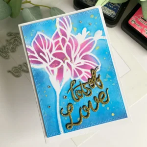 Handmade spring flower card with lot's of love Angled top-down view of the handmade spring flower card lying flat, capturing the layered ink blending of the flower and background. The gold shadowed sentiment stands out against the deep blue, and the dimension from the foam tape adds subtle depth.