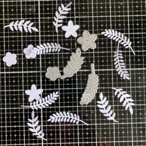 Die-cut leaves A flat lay image of leaf dies and their white die-cut shapes. The cutouts are ready for ink blending as part of the tunnel card tutorial. Two different styles of leaves are visible, offering texture and variation for scene building.