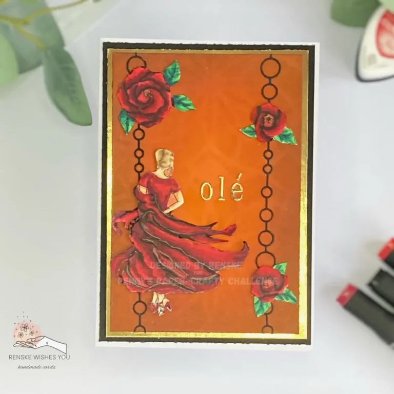 Top-down photo of a handmade card featured in the flamenco dancing card tutorial. The card has a deep orange background with a subtle stencilled pattern and bold black chain-like die-cut borders running vertically on both sides. A flamenco dancer in a flowing red and burgundy dress is positioned off-centre, mid-movement. Gold foil sentiment “olé” is placed to the right of the dancer. Red roses with green leaves are placed at the top left, middle right, and bottom right, overlapping the chain elements. The card is framed with a narrow gold layer and a white card base. In the background, alcohol markers and eucalyptus leaves are partially visible.